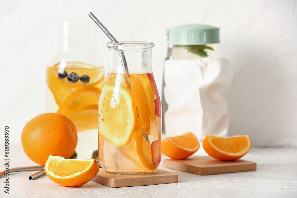 Bottles of infused water with orange slices on white table