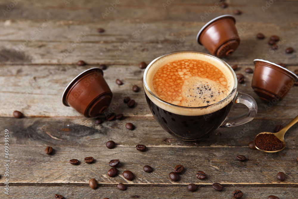 Cup of delicious coffee, capsules and beans on wooden table