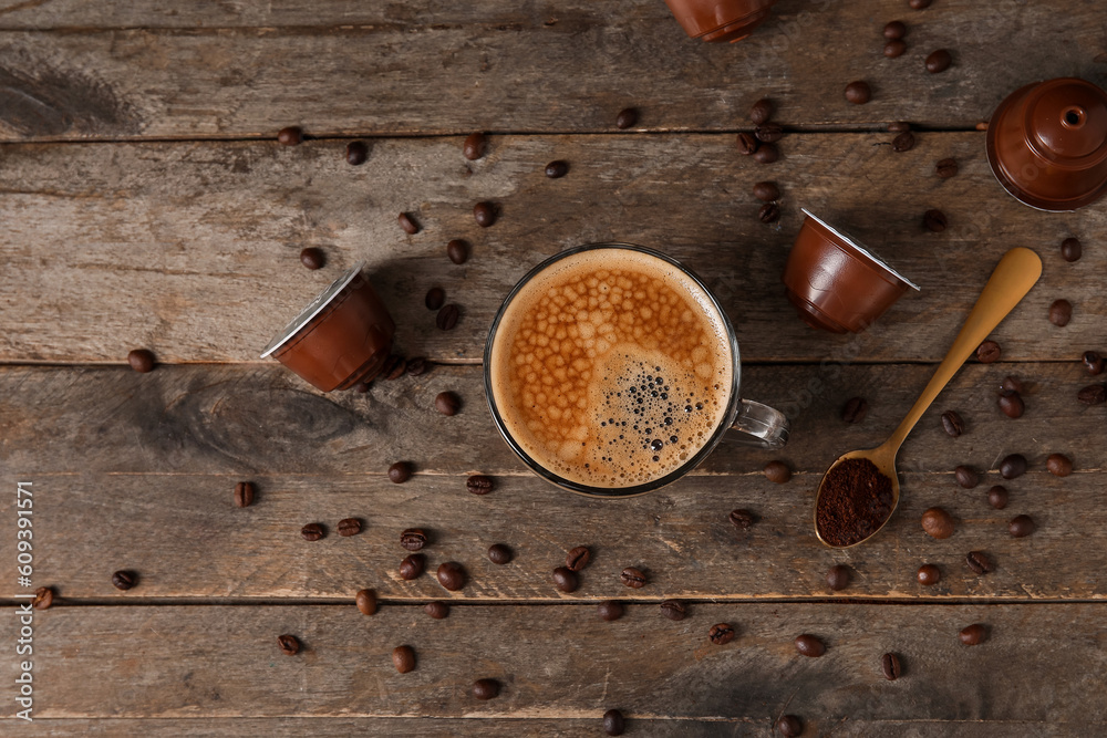 Cup of delicious coffee, capsules and beans on wooden table