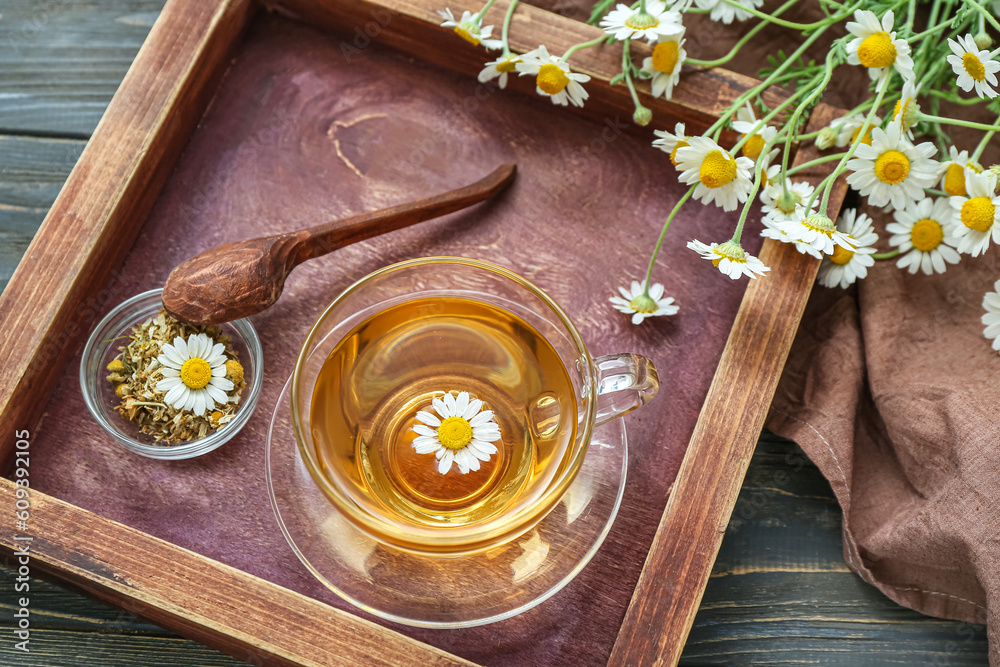 Cup of hot chamomile tea on dark wooden background