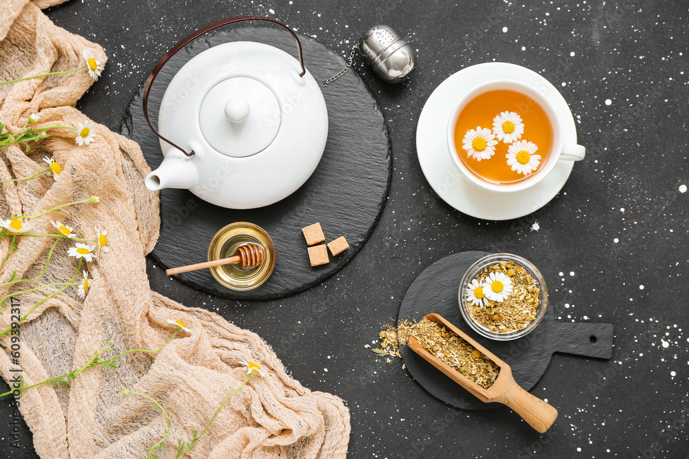 Cup of hot chamomile tea and teapot on dark background