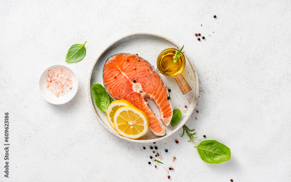 Fresh raw salmon steaks with spices, lemons and pink salt on white plate. Top view of fish on white 