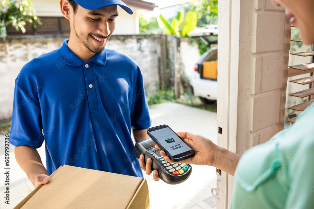 Asian young delivery man in blue uniform delivering package to customer. 