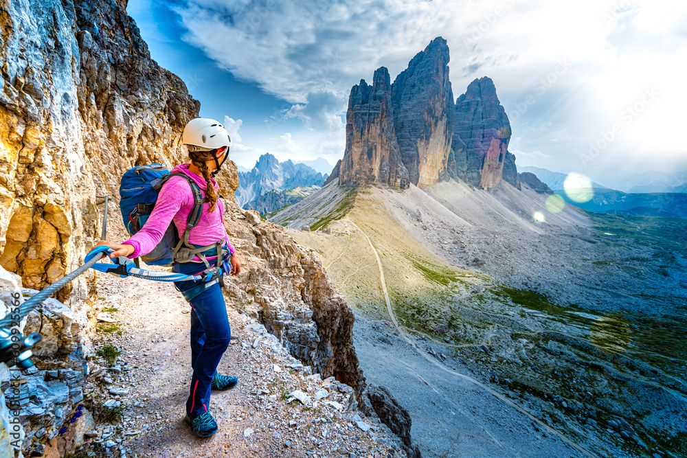 Young athletic woman enjoys scenic view on Tre Cime from via ferrata in the evening. Tre Cime, Dolom