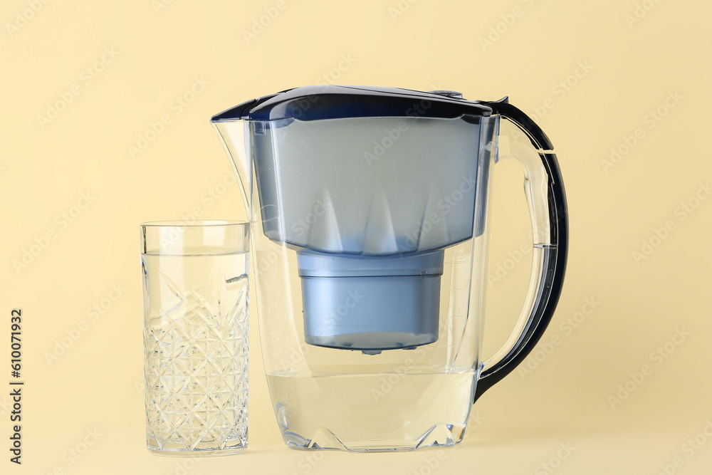 Water filter jug with glass on beige background