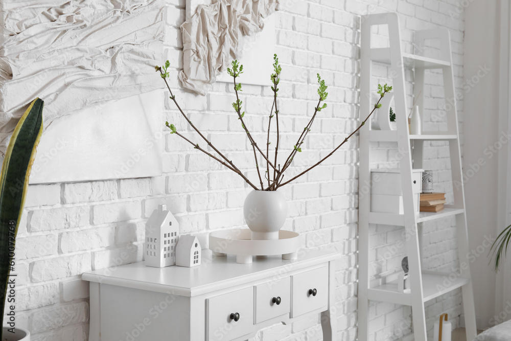 Vase with plant branches on table against light brick wall