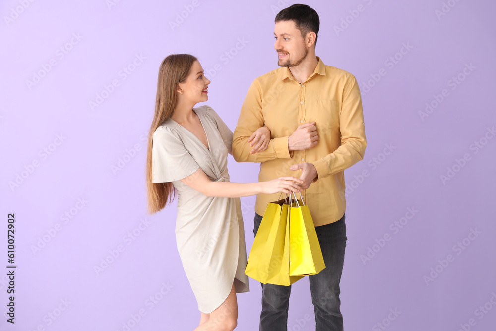 Lovely young couple with shopping bags holding hand in hand on lilac background