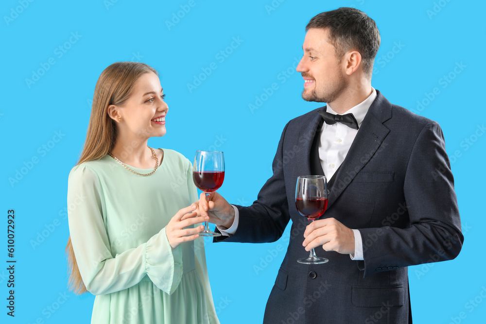 Young man in suit giving his wife glass of wine on blue background