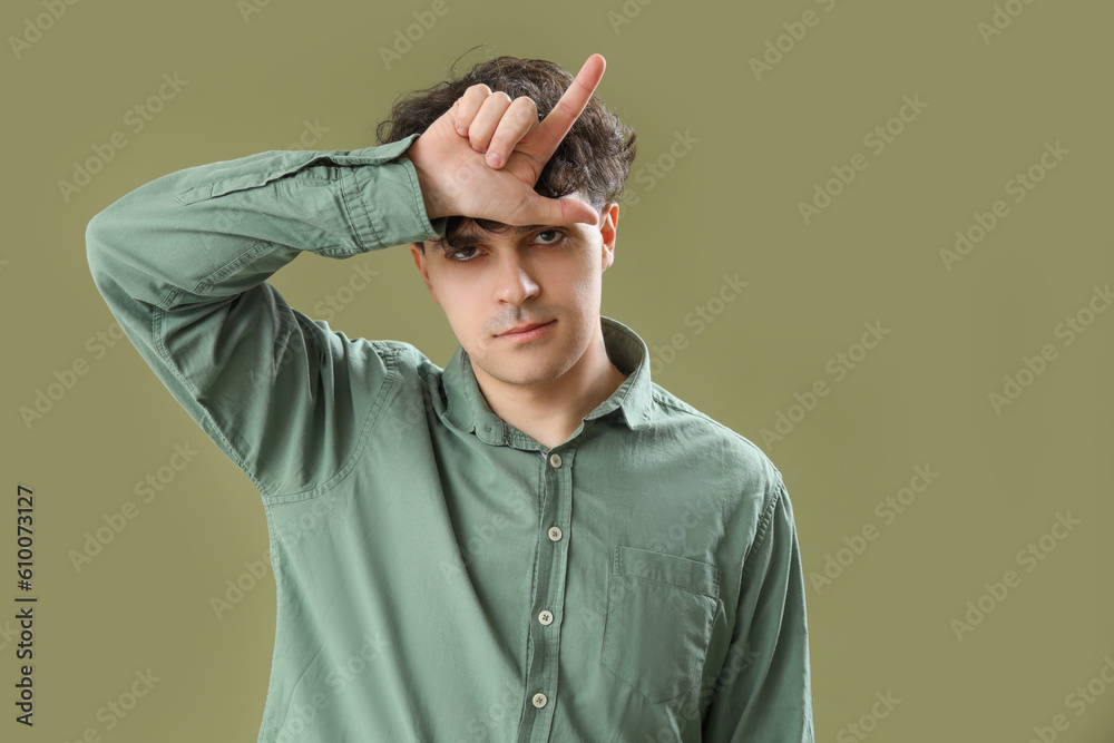 Sad young man showing loser gesture on green background