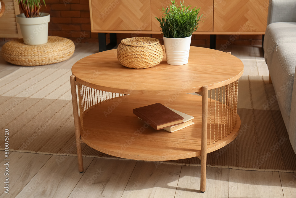 Wooden coffee table with houseplant, books and wicker basket in interior of living room