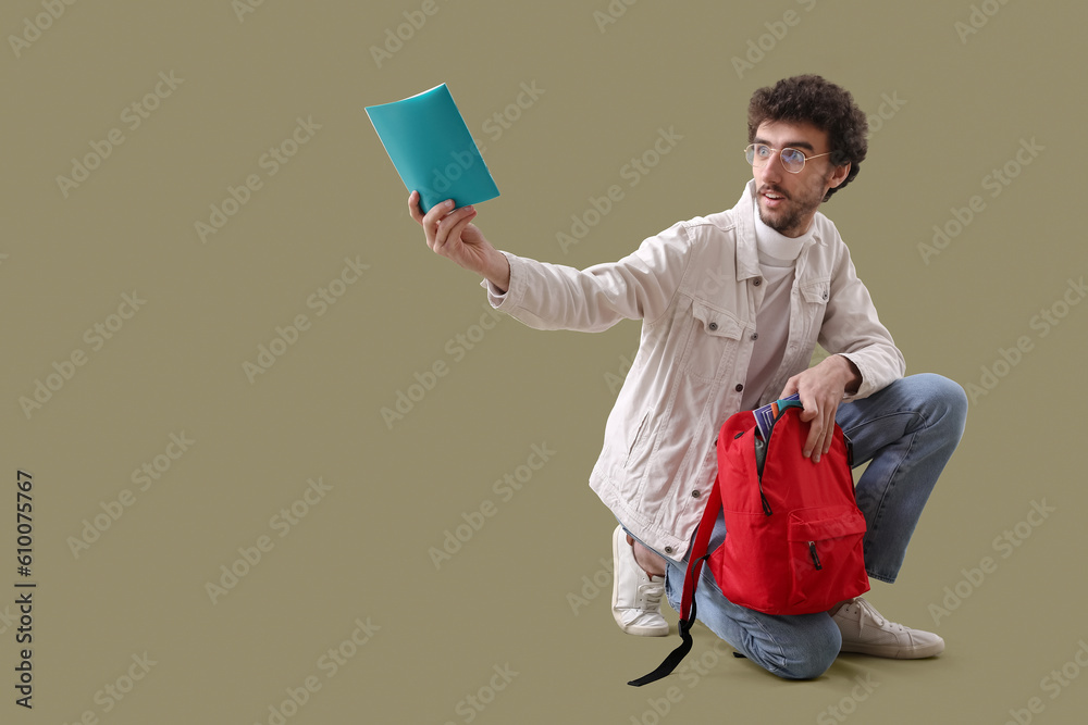 Male student with copybook and backpack on green background