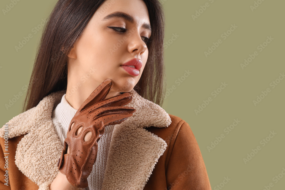 Stylish young woman in leather gloves on green background, closeup