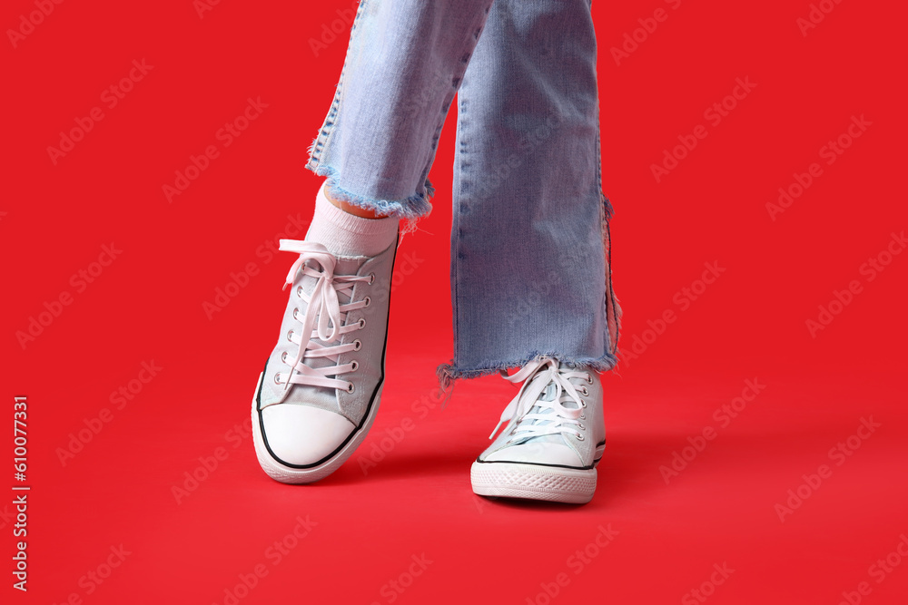 Female legs in stylish gumshoes on red background, closeup