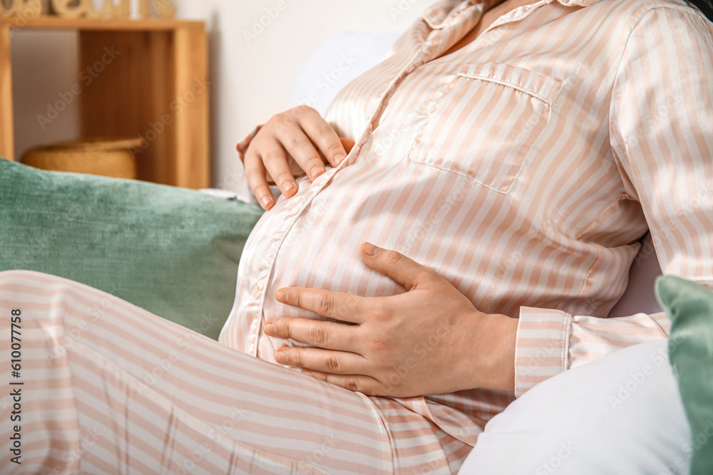 Young pregnant woman sitting in bedroom, closeup