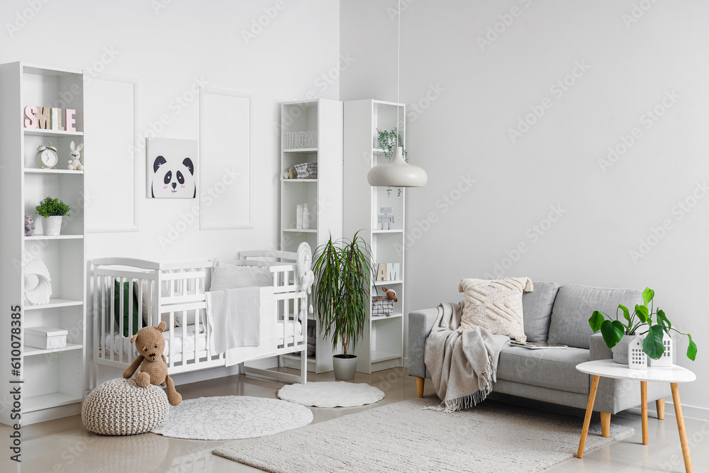 Stylish interior of childrens room in white tones with baby bed and shelving unit