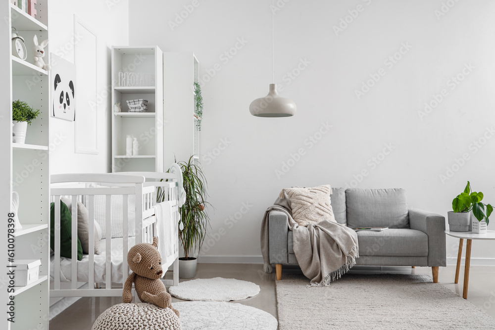 Stylish interior of childrens room in white tones with baby bed and shelving unit