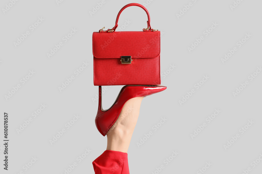 Female leg in red high heels with bag on grey background