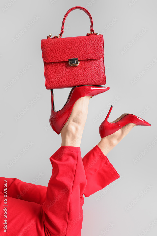 Female legs in red high heels with bag on grey background