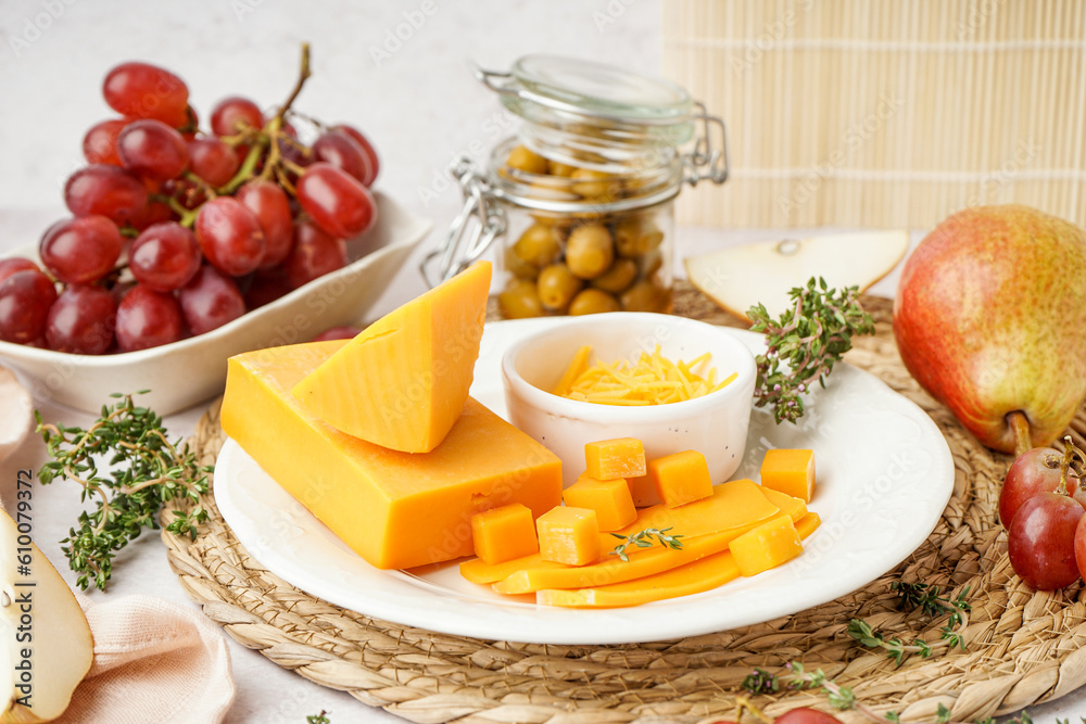 Plate with tasty cheddar cheese, grapes and olives on light background