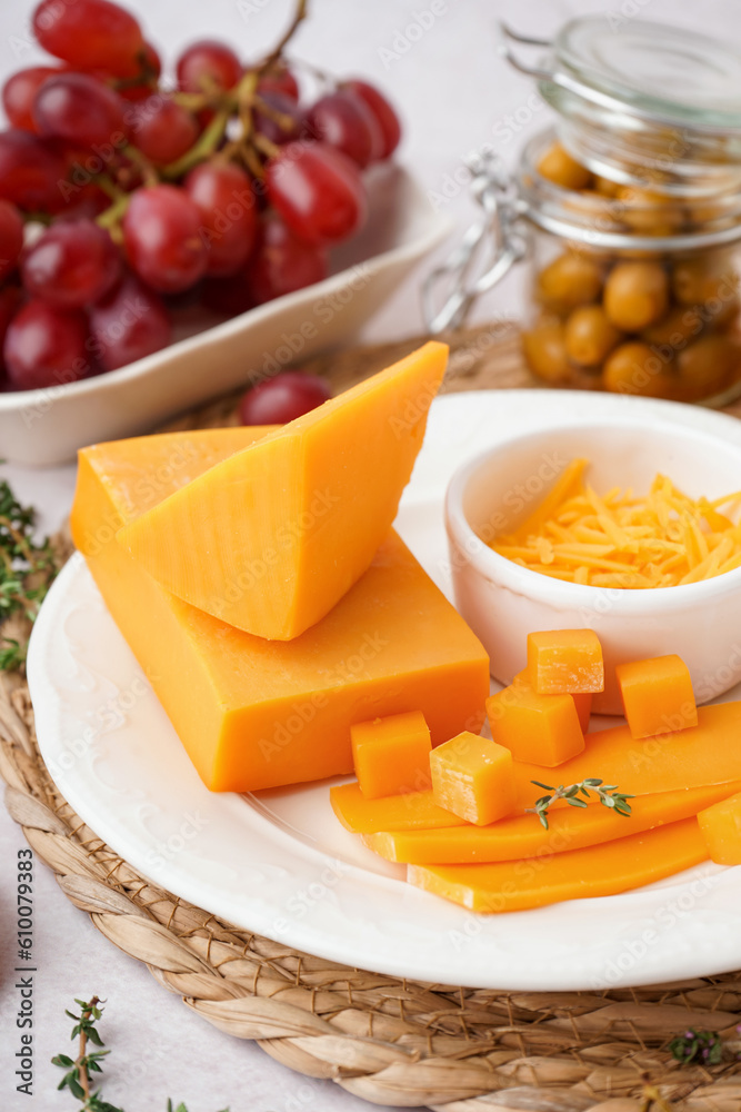 Plate with tasty cheddar cheese, grapes and olives on light background, closeup