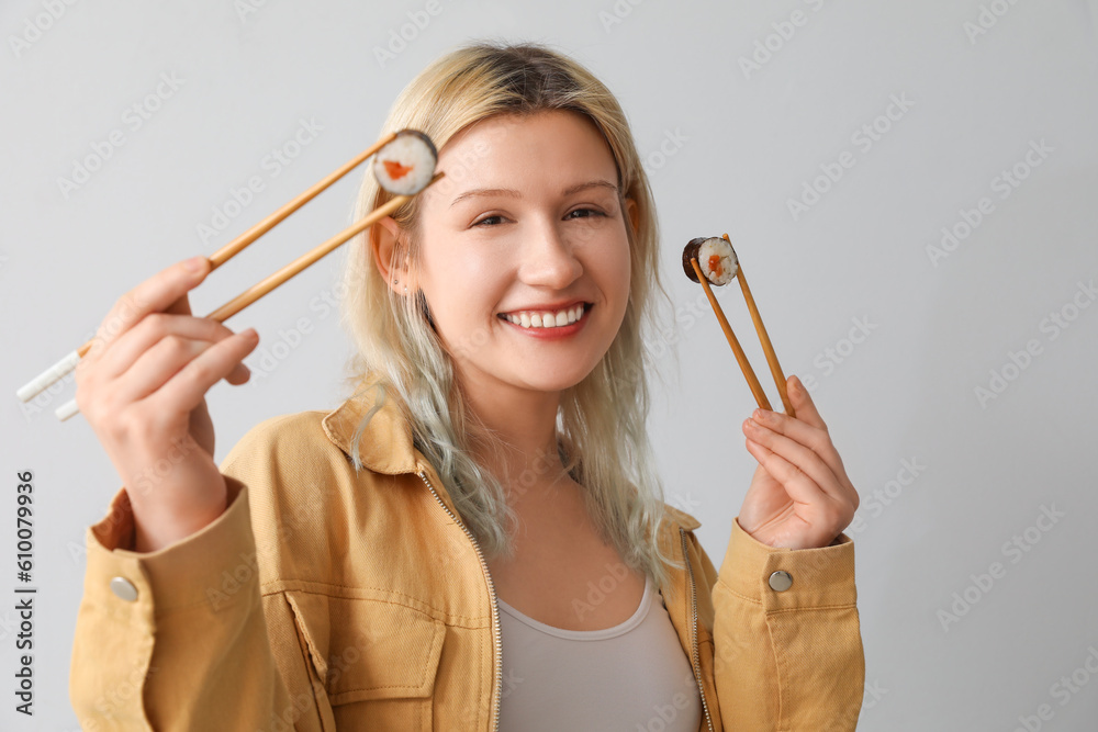 Young woman with sushi rolls on light background, closeup