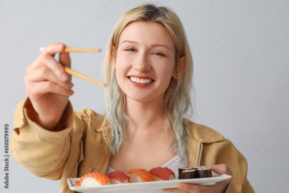 Young woman with sushi and chopsticks on light background, closeup