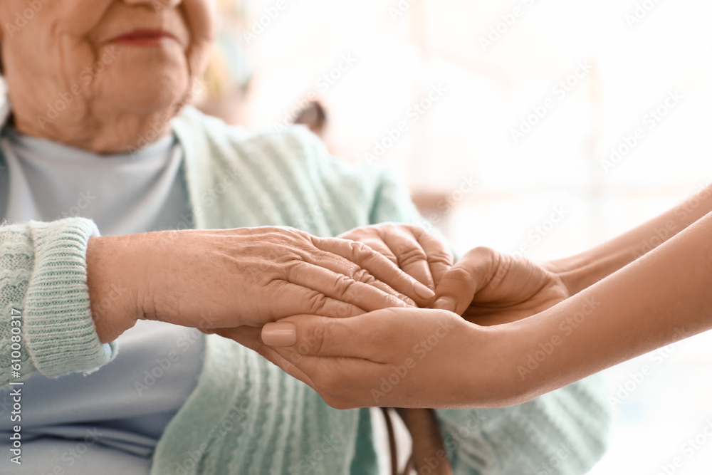 Senior woman with her granddaughter holding hands at home, closeup