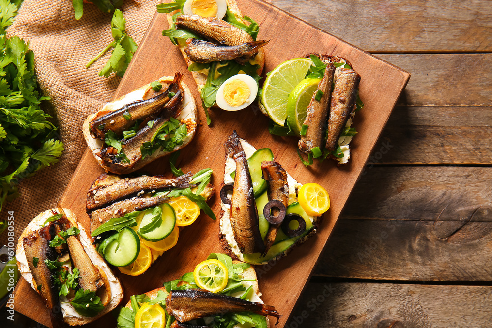 Board of tasty sandwiches with canned smoked sprats on wooden background