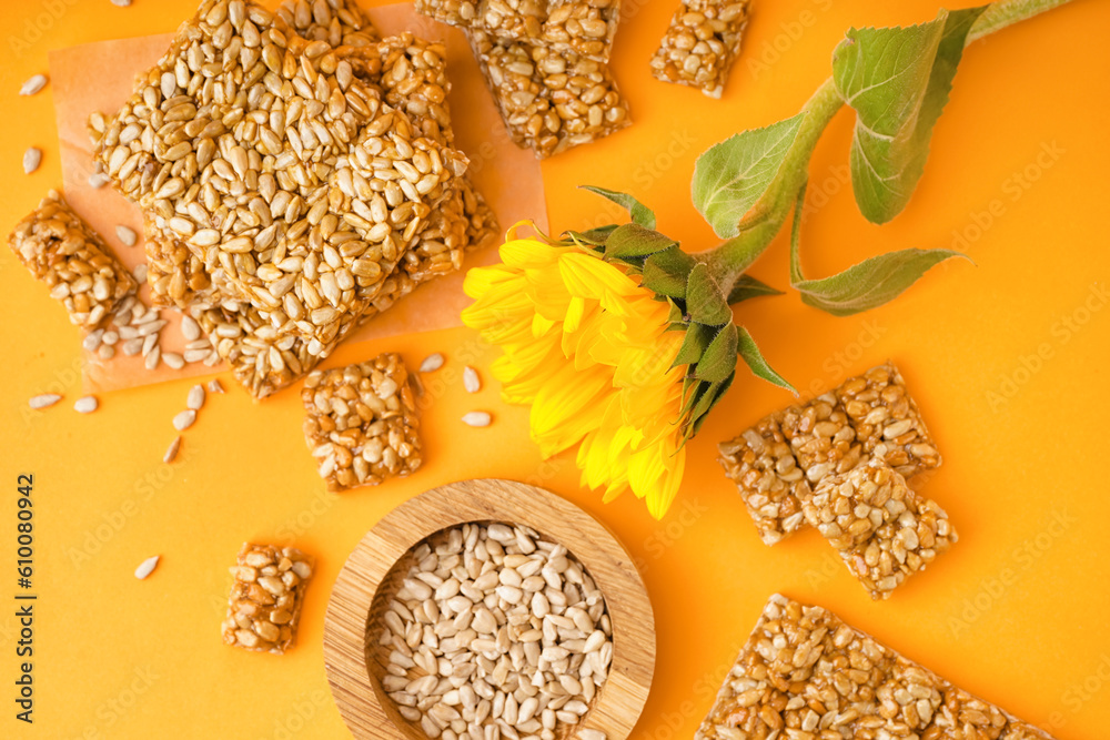 Wooden bowl of seeds with sunflower and tasty kozinaki on orange background