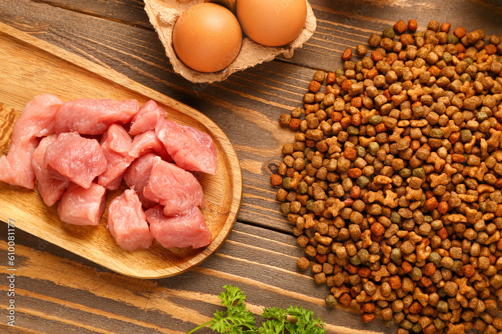 Dry pet food, raw meat and natural products on wooden background