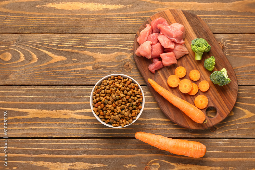 Bowl with dry pet food, raw meat and natural products on wooden background