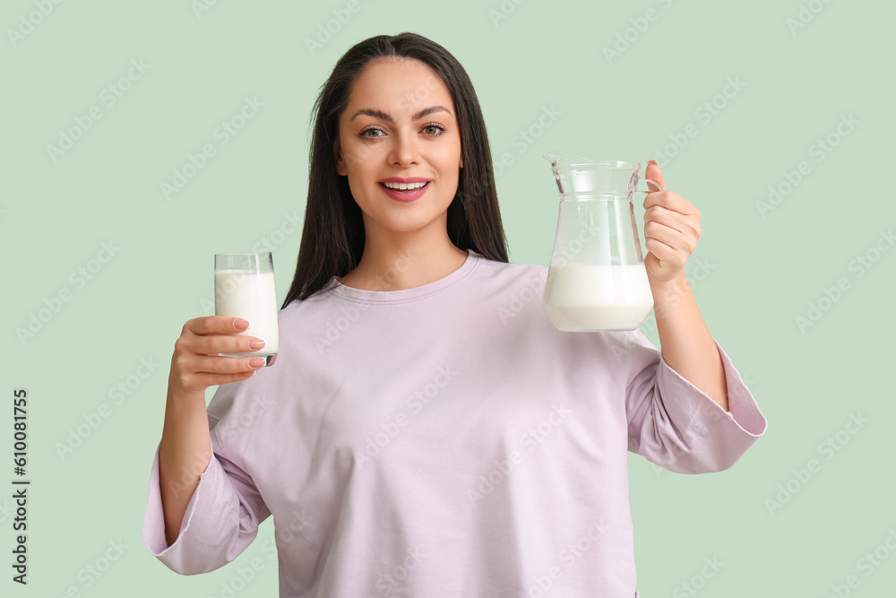 Beautiful young woman with glass and jug of milk on mint background