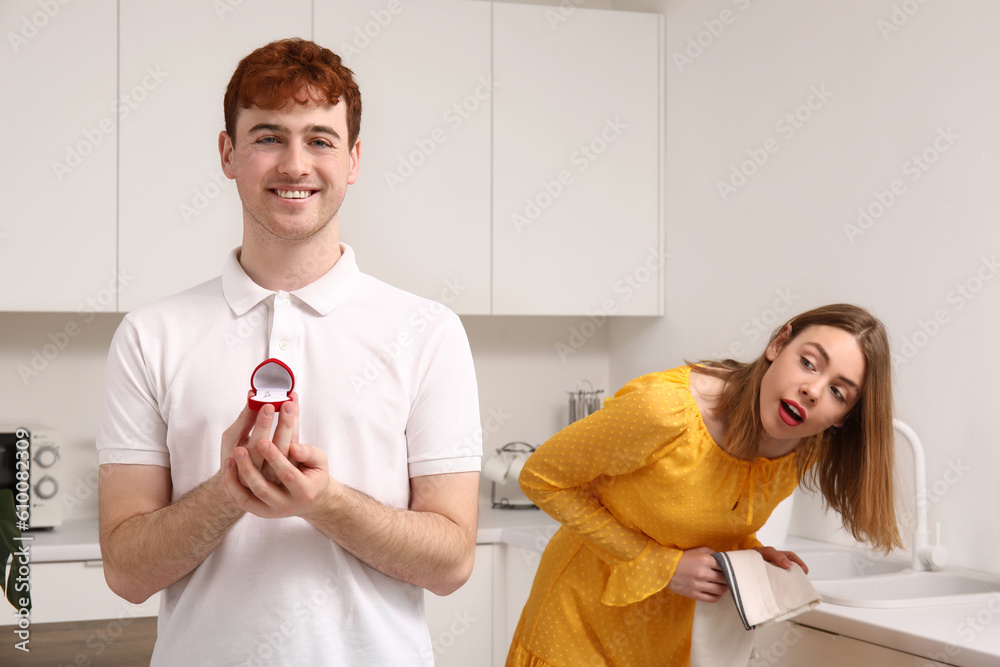 Young man with engagement ring and his curious girlfriend in kitchen