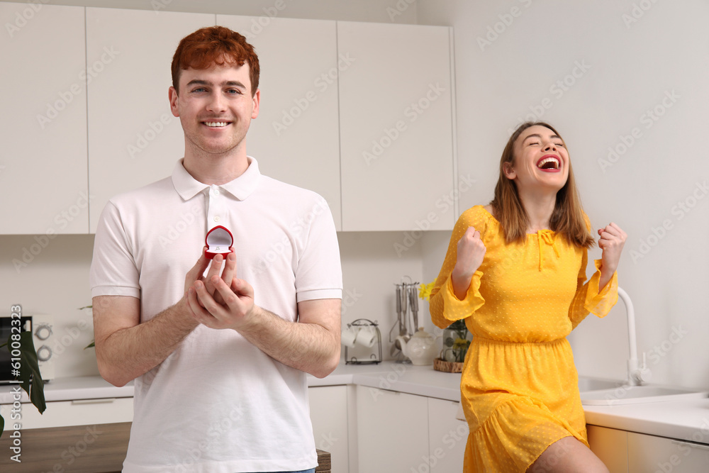 Young man with engagement ring and his happy girlfriend in kitchen