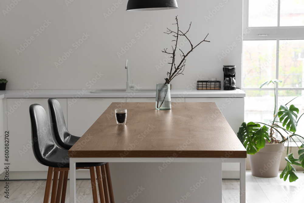 Vase with tree branches and glass of coffee on island in modern kitchen