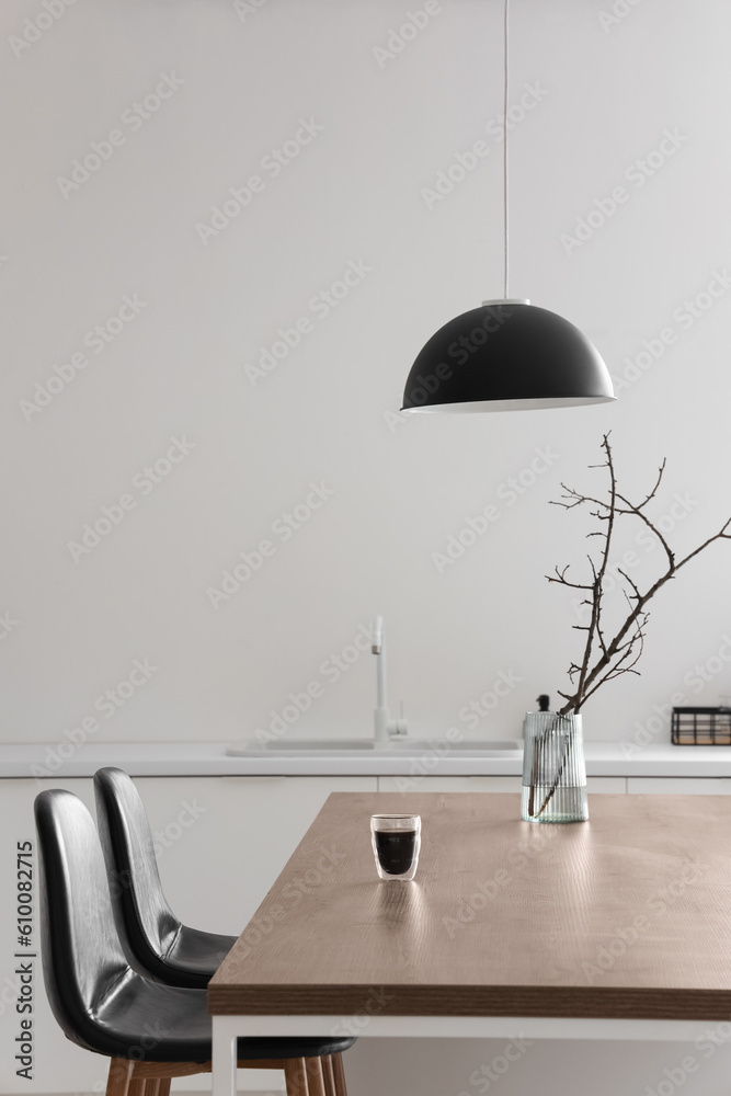 Vase with tree branches and glass of coffee on island in modern kitchen