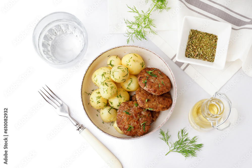 Bowl with cutlets, boiled baby potatoes and dill on white table in kitchen