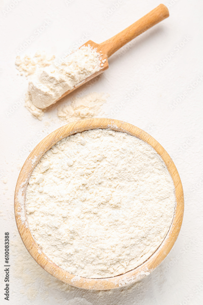 Wooden bowl with wheat flour and scoop on white background