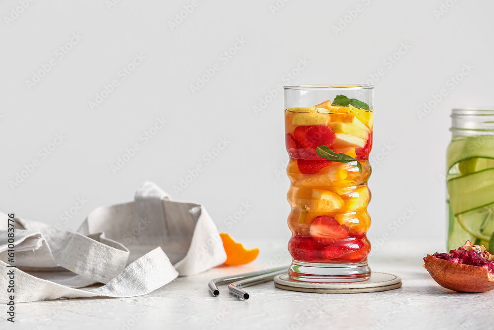 Glass and mason jar of infused water with different sliced fruits on white table