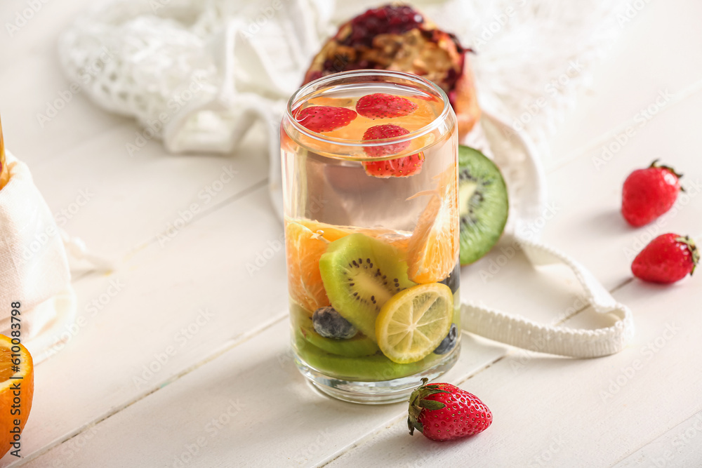 Glass of infused water with different sliced fruits on white wooden table