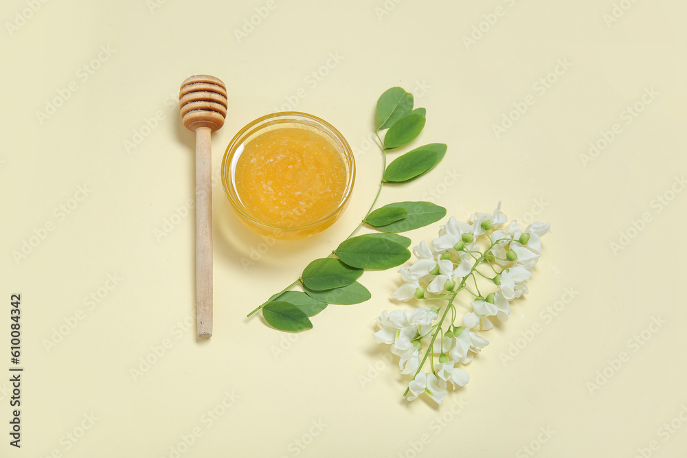 Bowl of honey with flowers of acacia and dipper on beige background