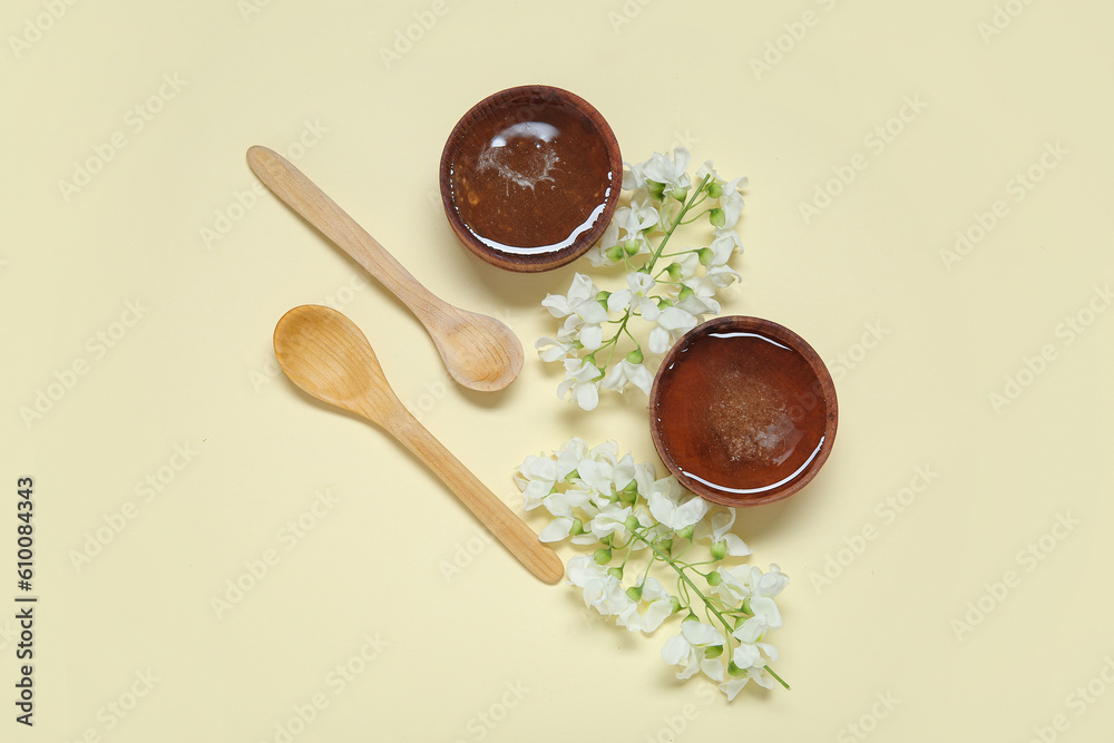 Bowls of honey with flowers of acacia and spoons on beige background