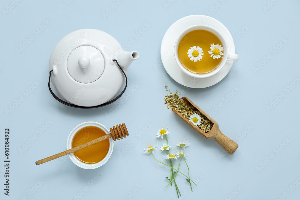 Teapot and cup of hot chamomile tea with honey on pale blue background