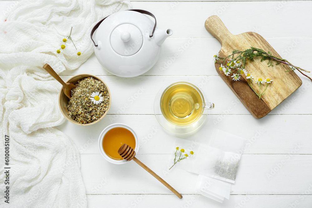 Teapot and cup of hot chamomile tea with honey on white wooden background