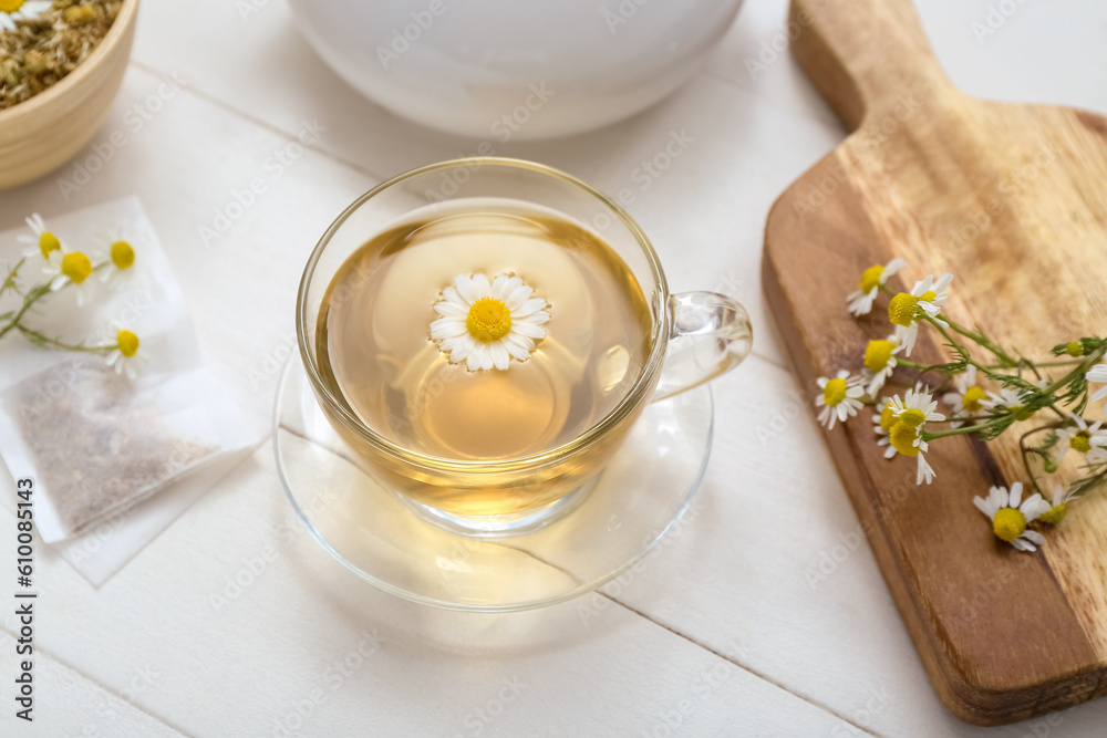 Board and cup of hot chamomile tea on white wooden background