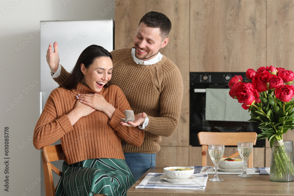 Young man proposing to his happy girlfriend in kitchen