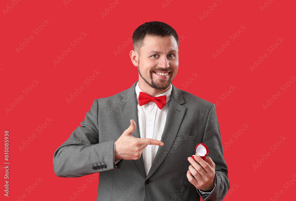 Handsome man with engagement ring on red background