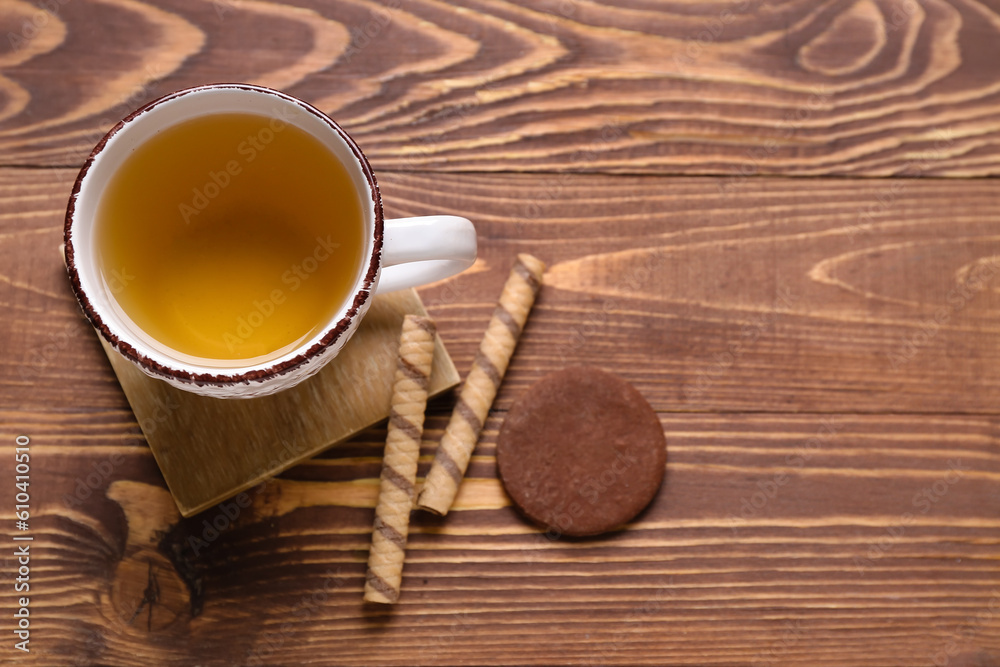 Drink coaster with cup of tea, wafer rolls and cookie on wooden table