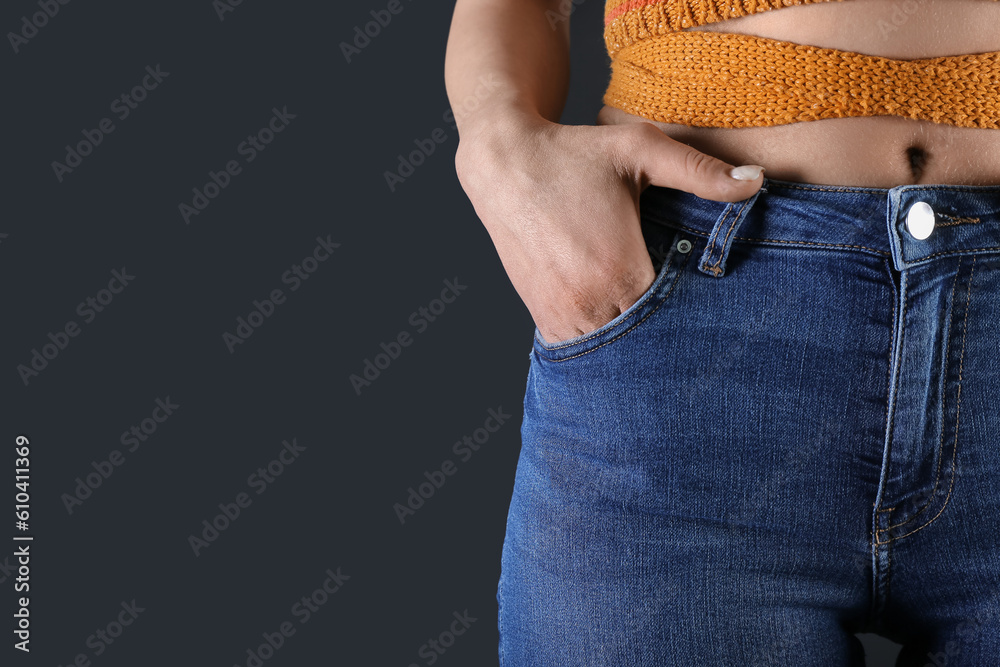 Young woman in skinny jeans on dark background, closeup