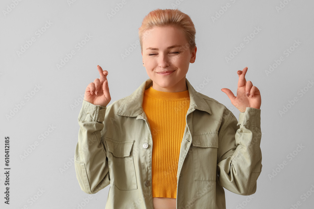 Young woman crossing fingers on light background